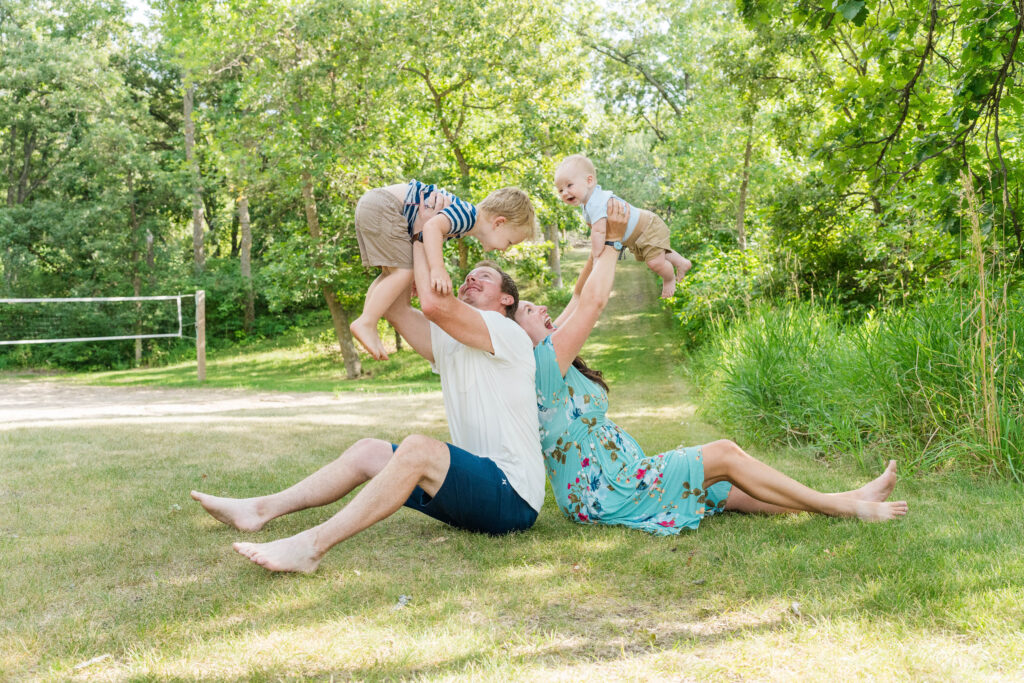 Family of Four sitting on the group lifting up their two little ones.