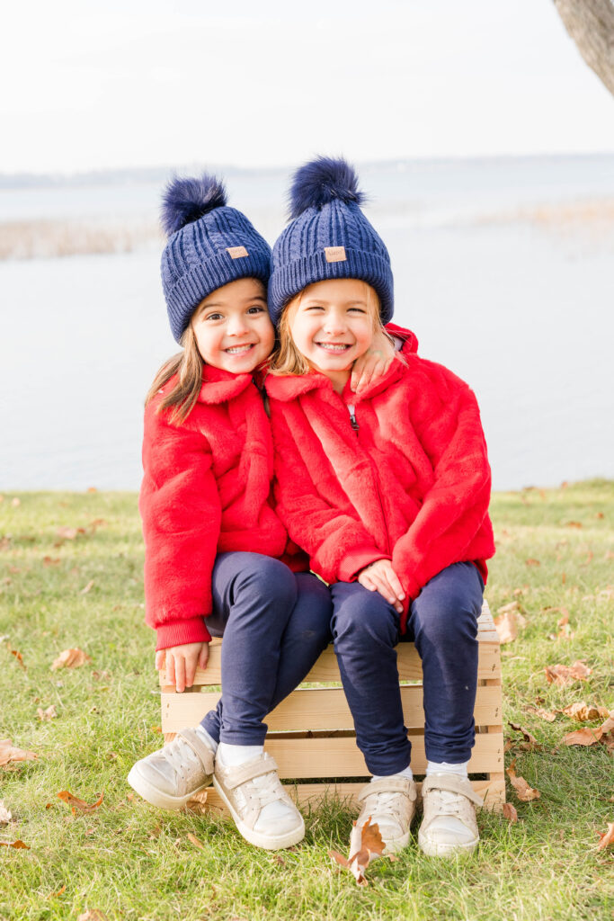 Two little girls wearing red sweaters and blue pom pom hats