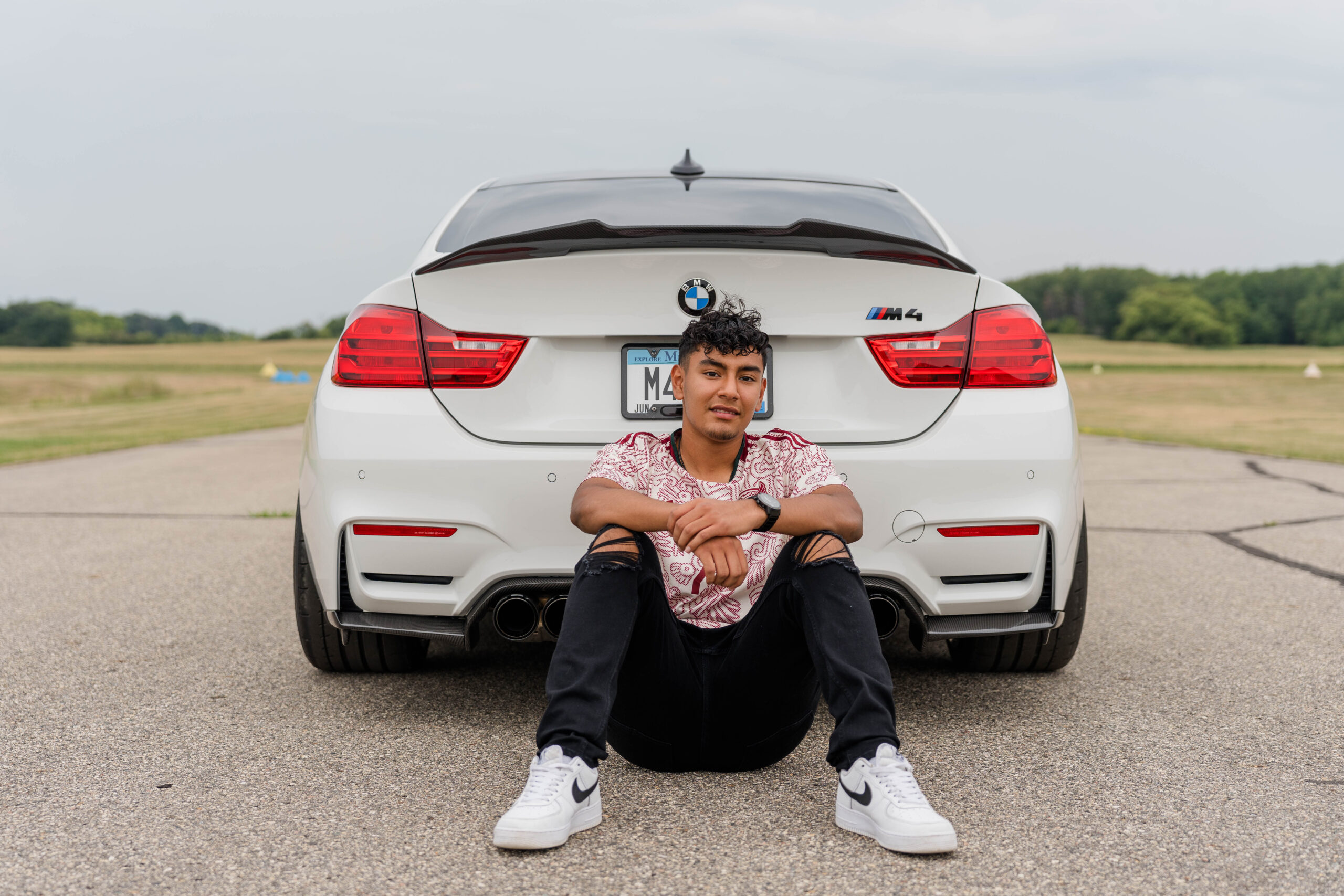 Graduating Senior leaning against his BMW M4.