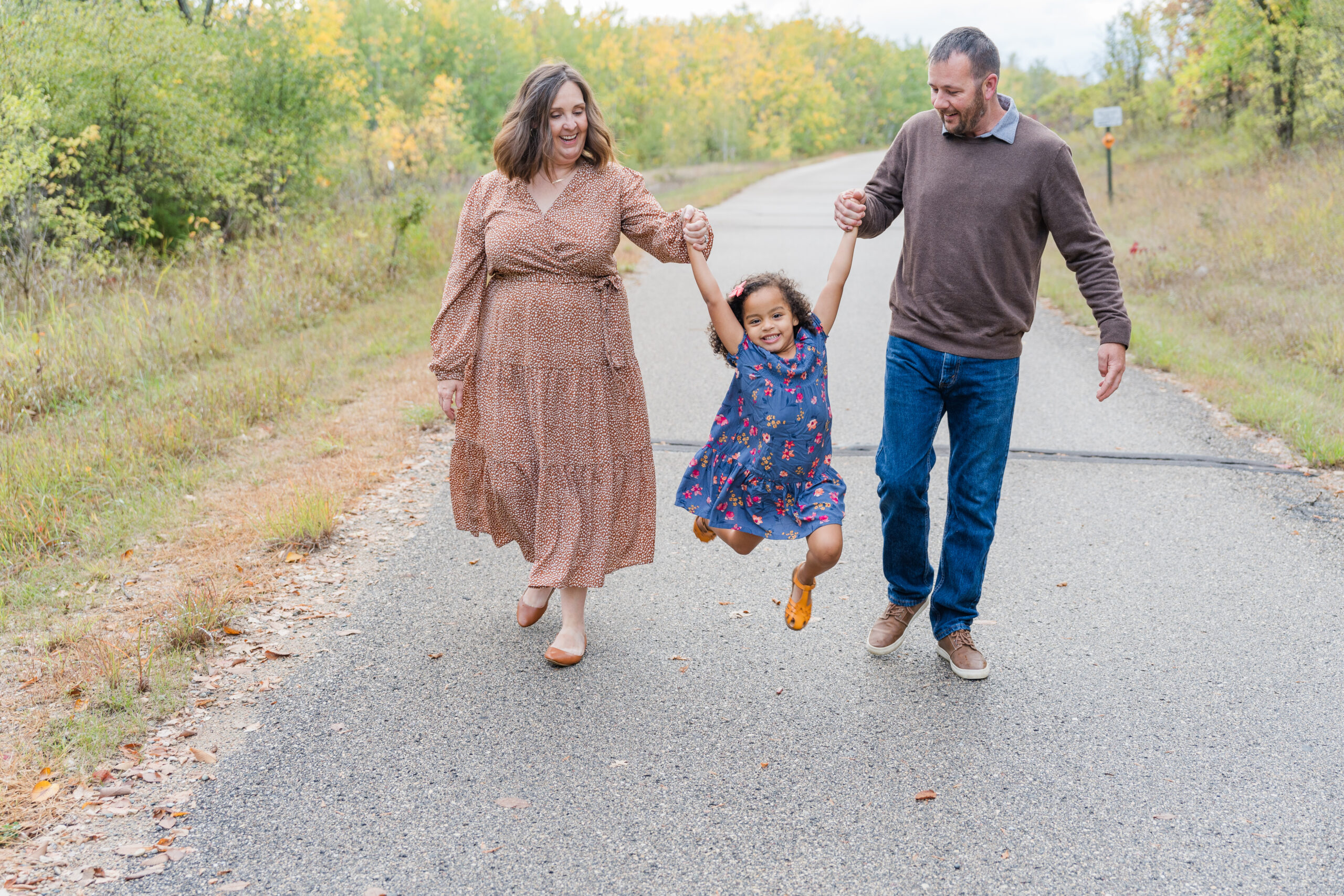 Family of Three swinging their little one between them on a paved path in Delagoon Park in Fergus Falls Minnesota