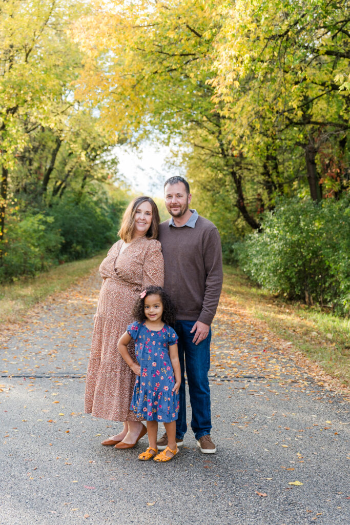 Family of three standing on a paved trail with the sun coming through the trees after a rainstorm.