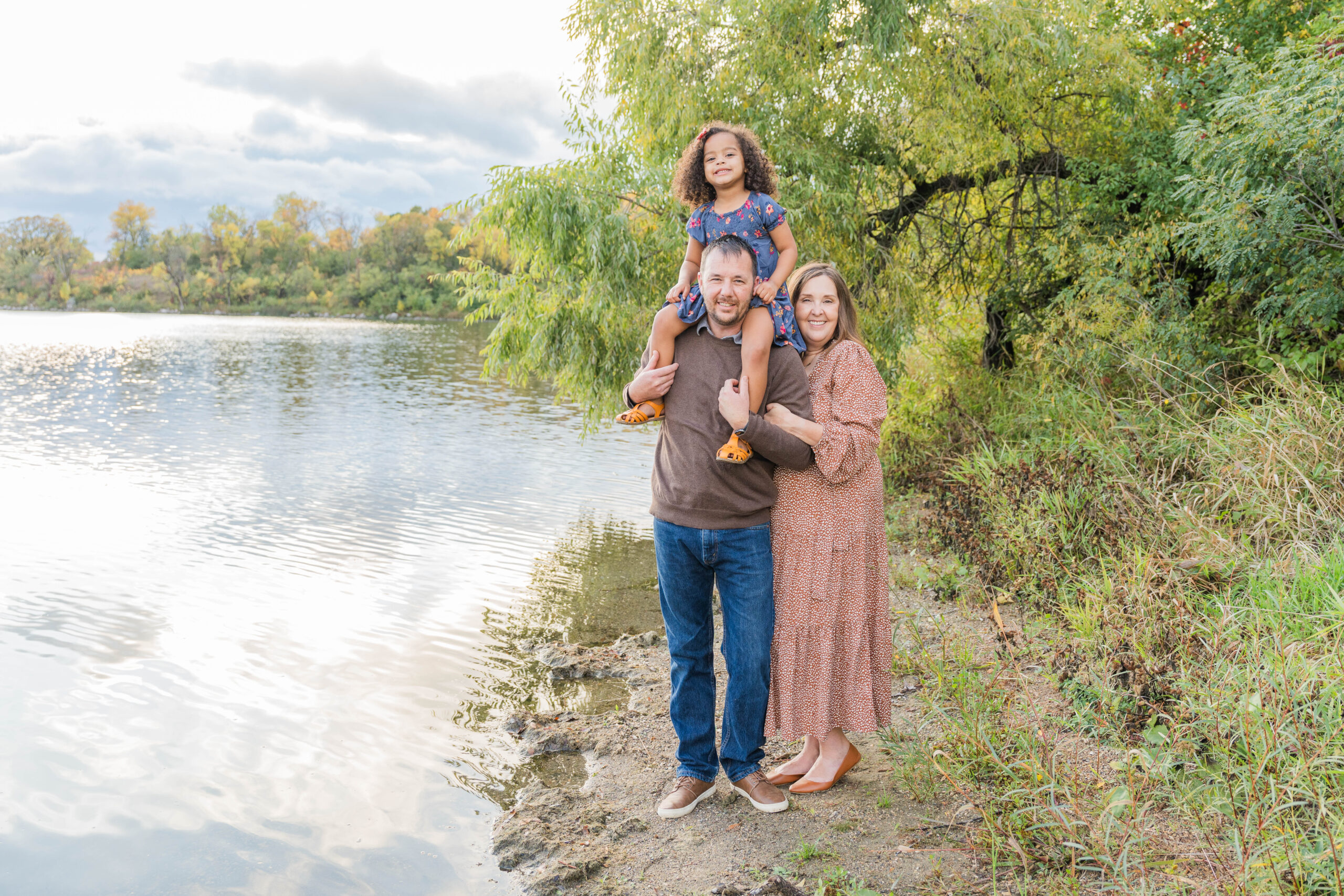 Family of Three, little girl sitting on top of her Dad's shoulders. Standing in front of a lake in Fergus Falls, MN