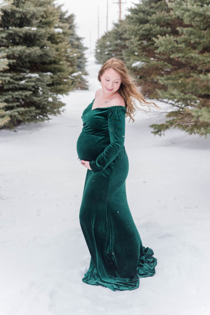 Pregnant Woman wearing a green dress standing in the snow.