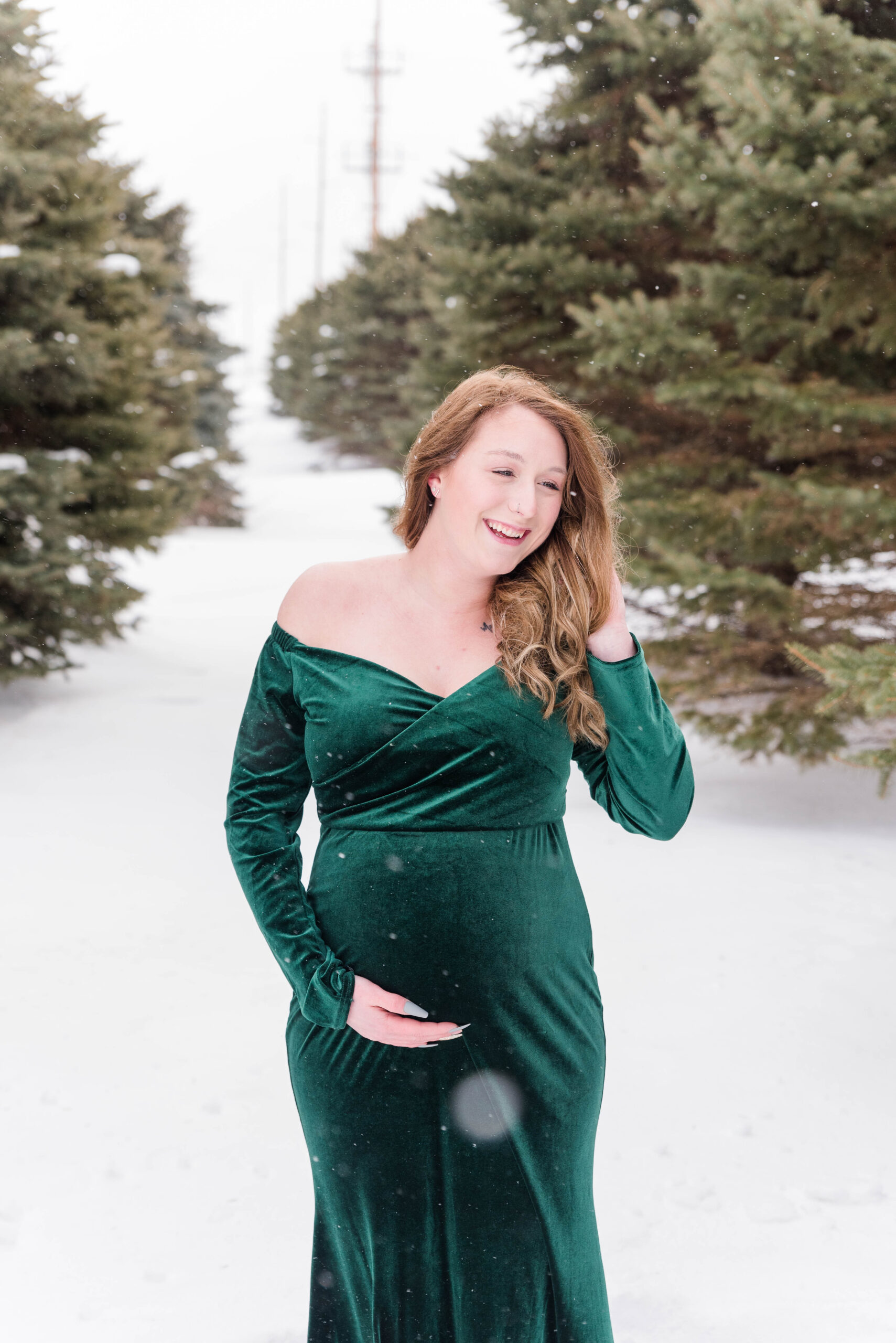 Pregnant woman wearing a green dress standing in the snow for a winter maternity session