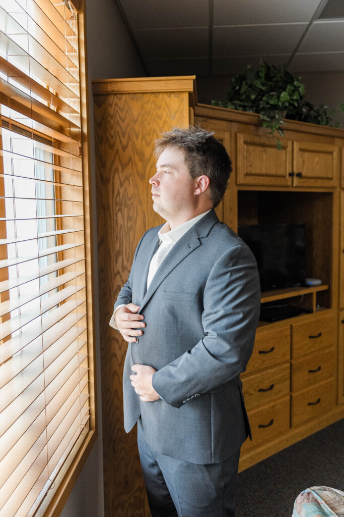 Groom standing in front of the window before his wedding. 