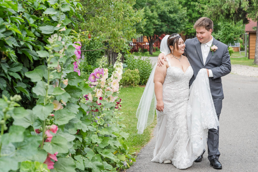 Bride and Groom walking together, he is holding her dress at Fair Hills Resort in Detroit Lakes, MN 